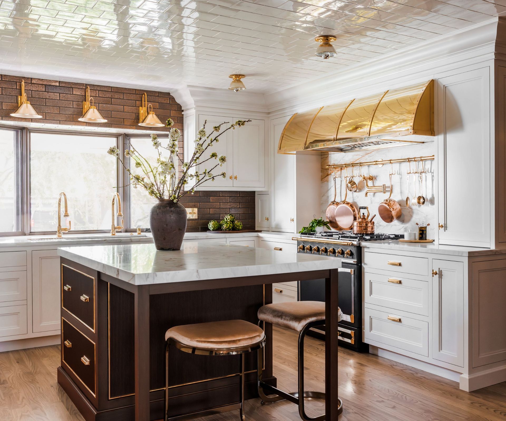 A white kitchen with shaker cabinets, gold accents, a dark brown island, and a tiled ceiling