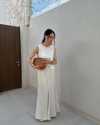 Woman wears a white silk drawstring waist dress and raffia flats.