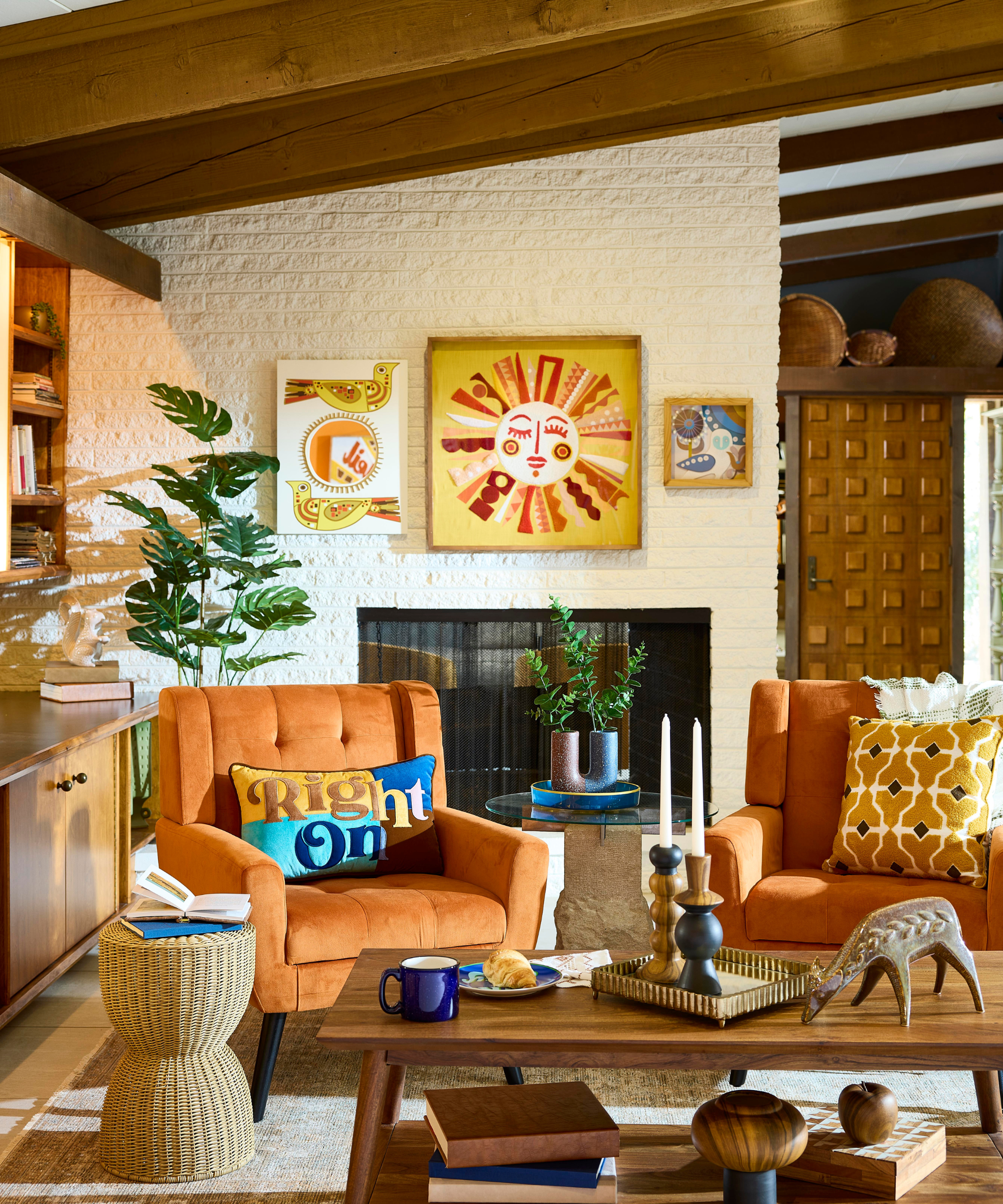 a mid-century style living room with artwork on the walls, orange accent chairs, and decor on the coffee table