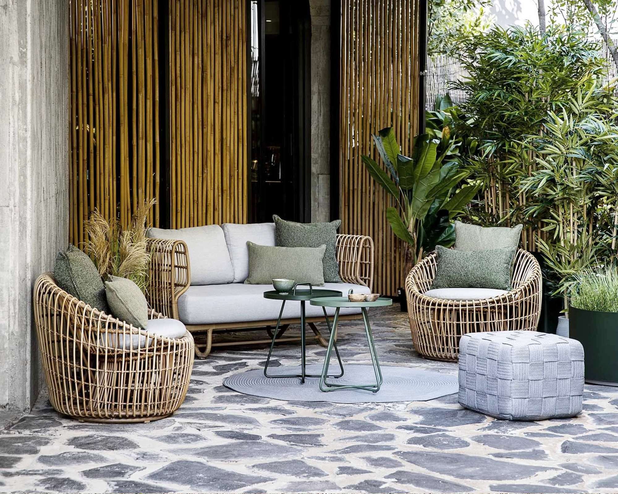 A wicker outdoor lounge set on a patio surrounded by tropical planting