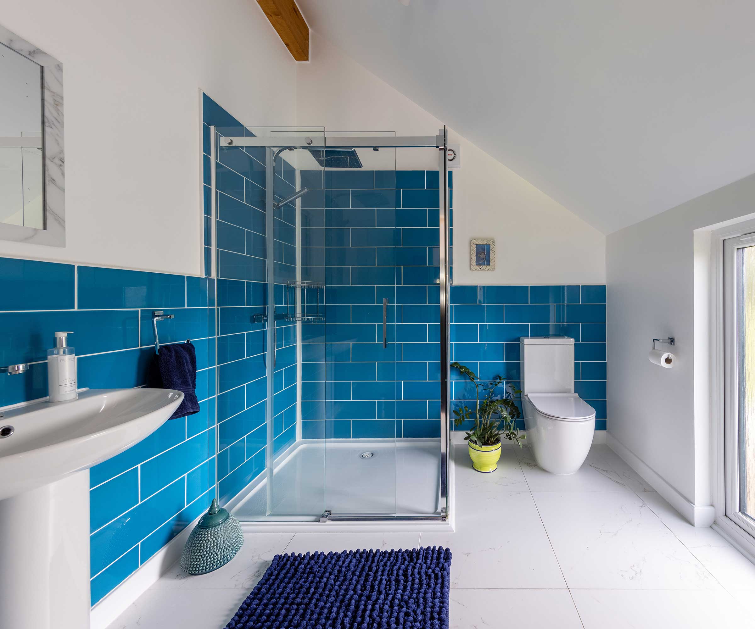 a bathroom with a sloping ceiling, white floor tiles, large shower enclosure and bright blue wall tiles