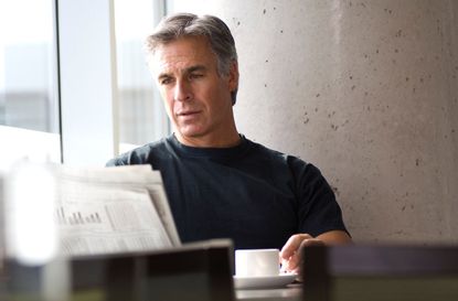 Gray haired middle aged man reading newspaper in cafe on weekend.