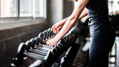 Woman selects dumbbells from the free weight section of a gym