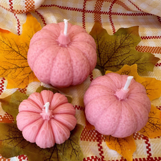 three pink candle pumpkins on an autumnal tablecloth