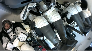 four astronauts in white space suits inside a cramped capsule cockpit