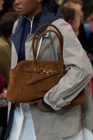 Nahaufnahme einer braunen Wildledertasche mit Ost-West-Griff auf der Miu Miu-Modenschau Frühjahr/Sommer 2025 in Paris.