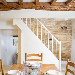 Dining area with wooden dining table and chairs and white staircase.