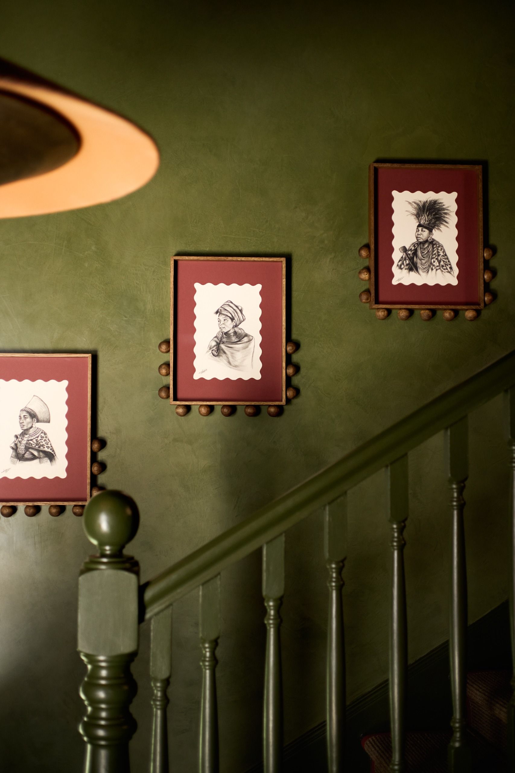 a green wall with burgundy framed art with small balls on the frame