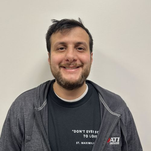 man smiling at the camera against a white background wearing a grey tshirt and hoodie.