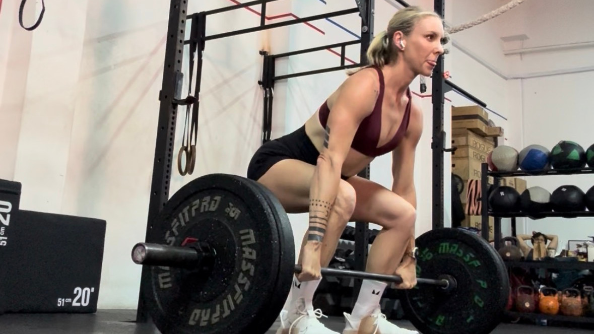 Amanda Lim performs a deadlift with a heavy barbell in a gym. 