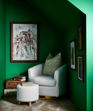 emerald green snug/cozy corner with cream boucle armchair and footstool, trunks/suitcaess and artwork