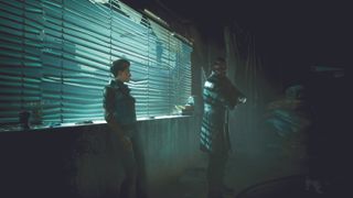 Solomon Reed and an NPC in a dark room with their backs to a window with blinds