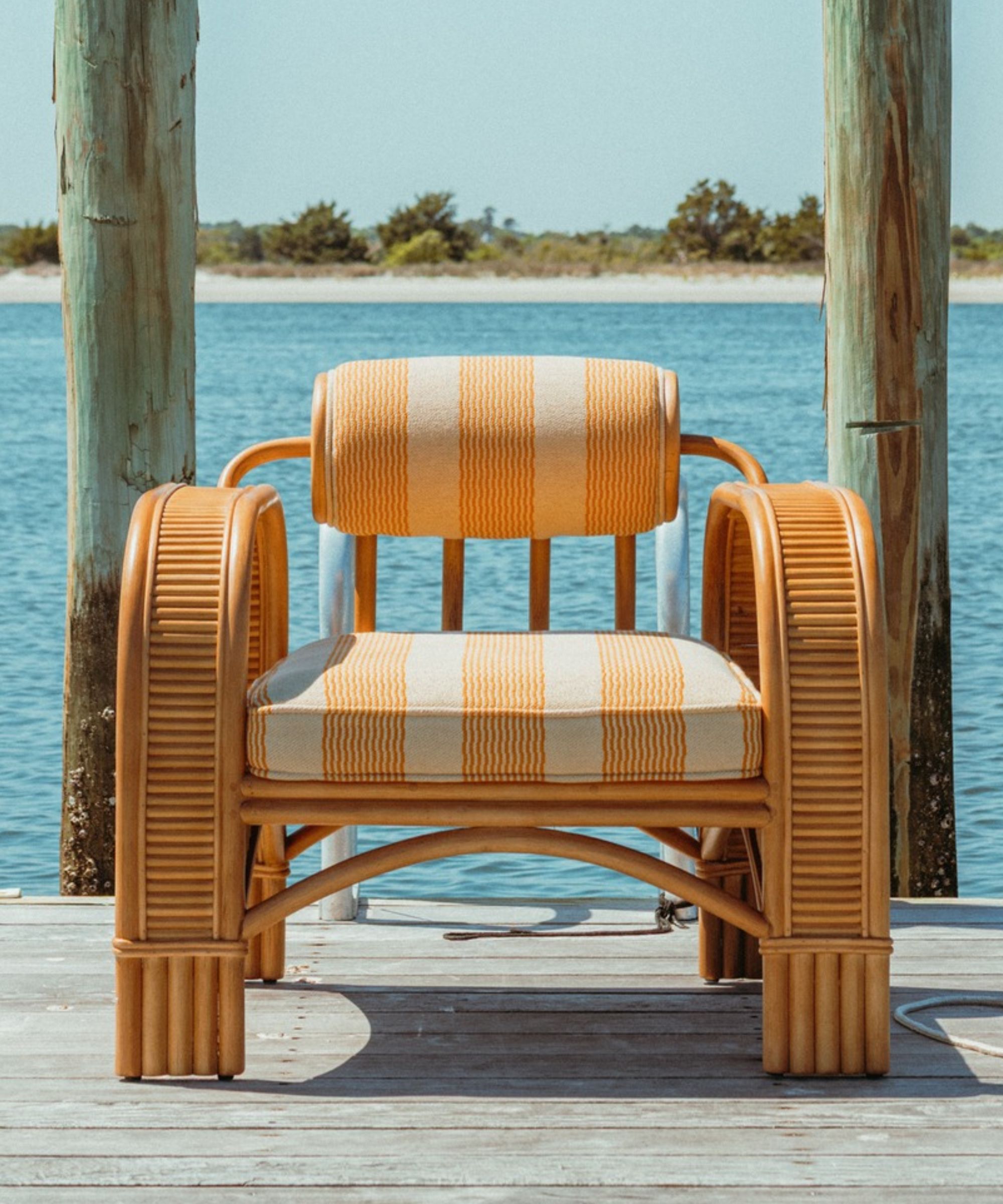 Yellow and white striped bamboo outdoor chair on jetty with water behind