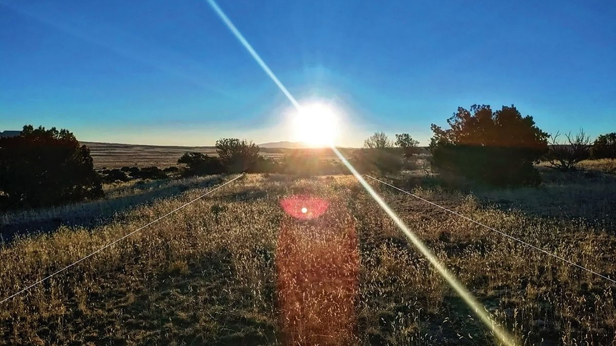 A sunrise over a grassy field with two white lines indicating a road drawn on the image