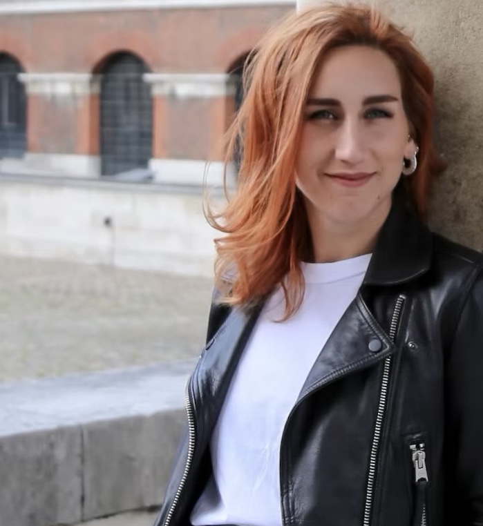 a woman with red hair and a leather jacket smiles.