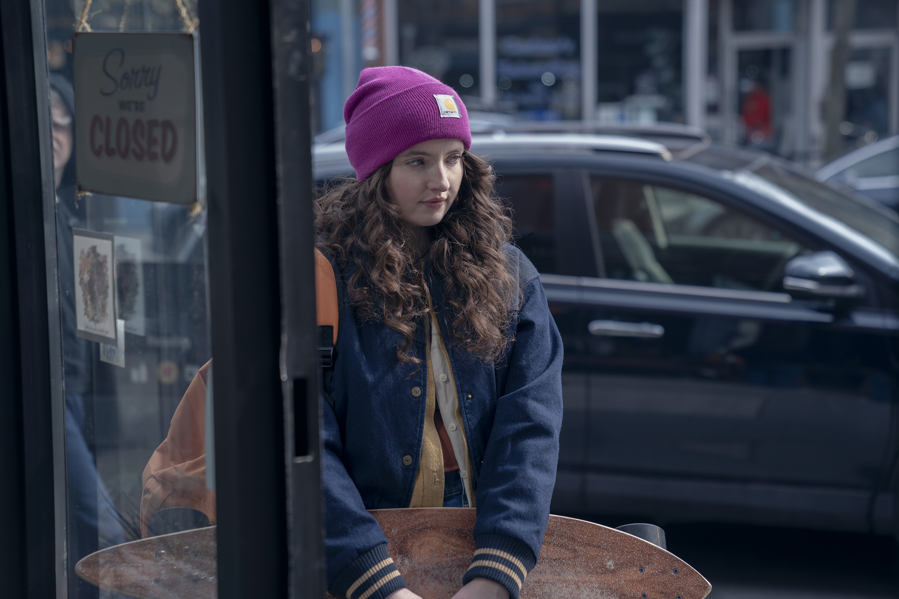 Lucy Halliday holds a skateboard outside a shop in 'The Testaments.'