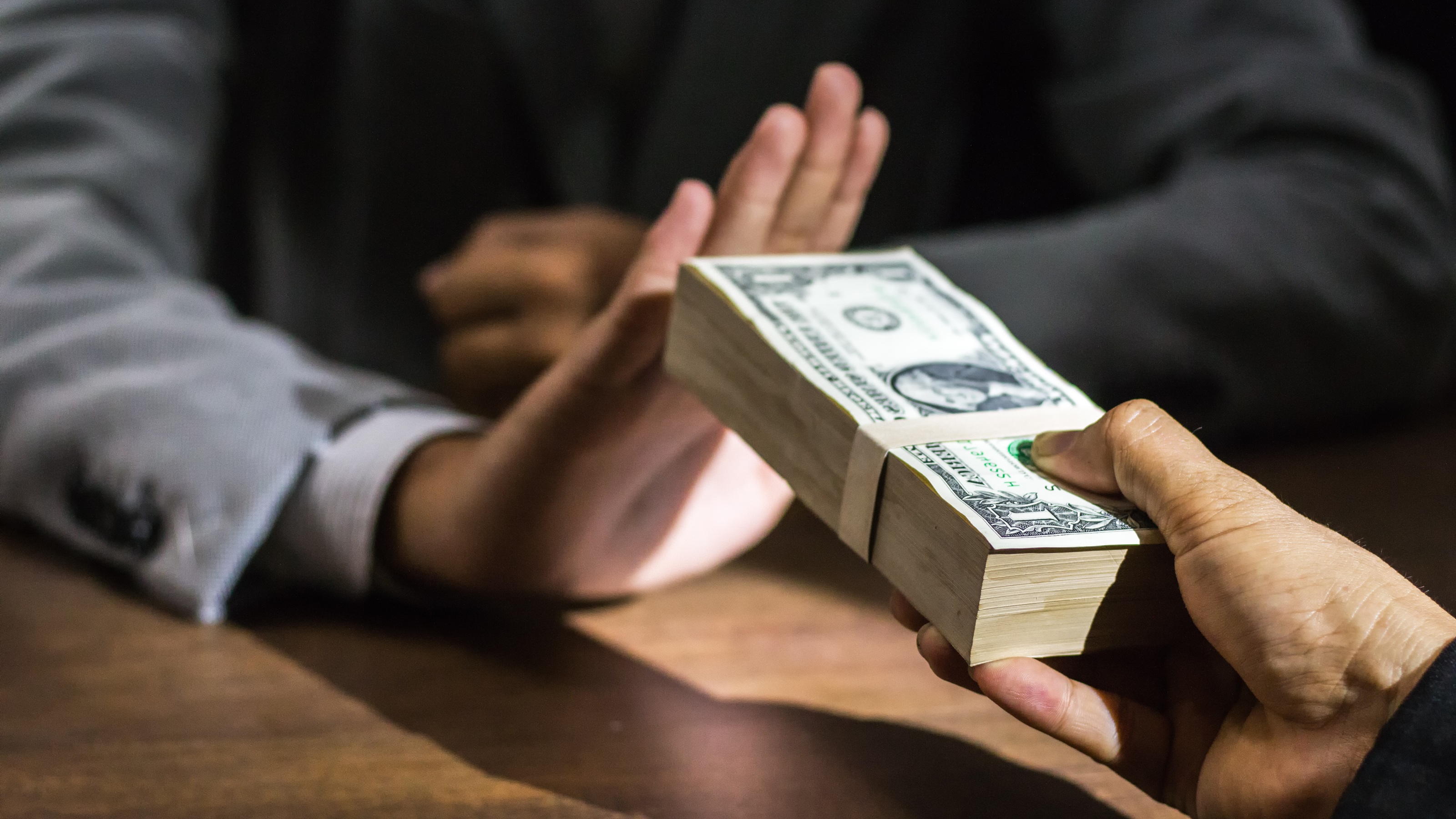 One man holds up a hand to refuse a stack of cash offered by another man.