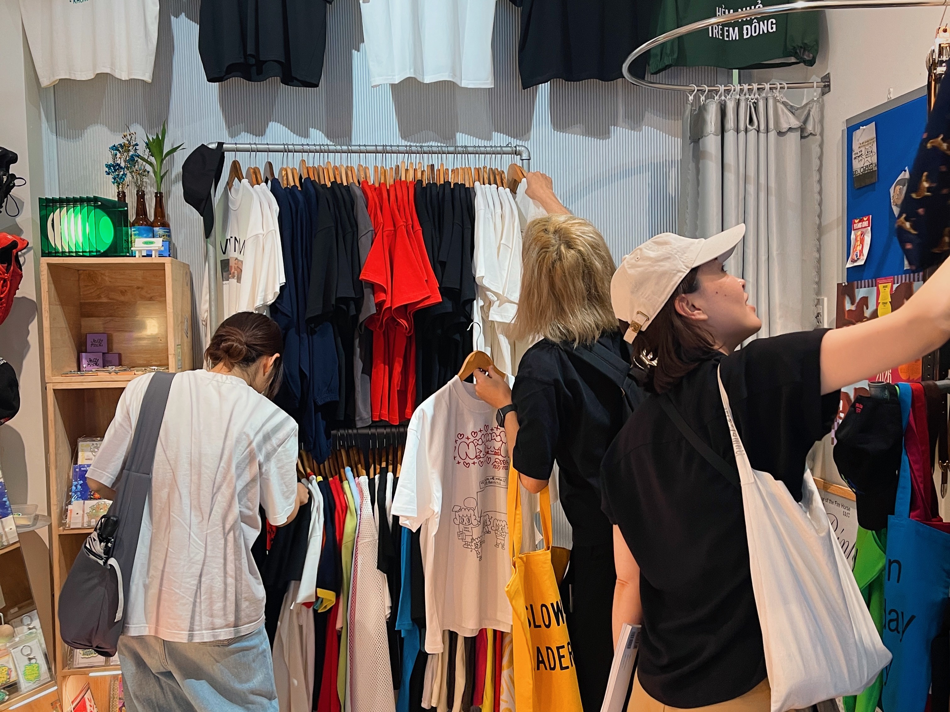 People shopping inside a thrift store packed with colorful T-shirts, accessories, and stationery.