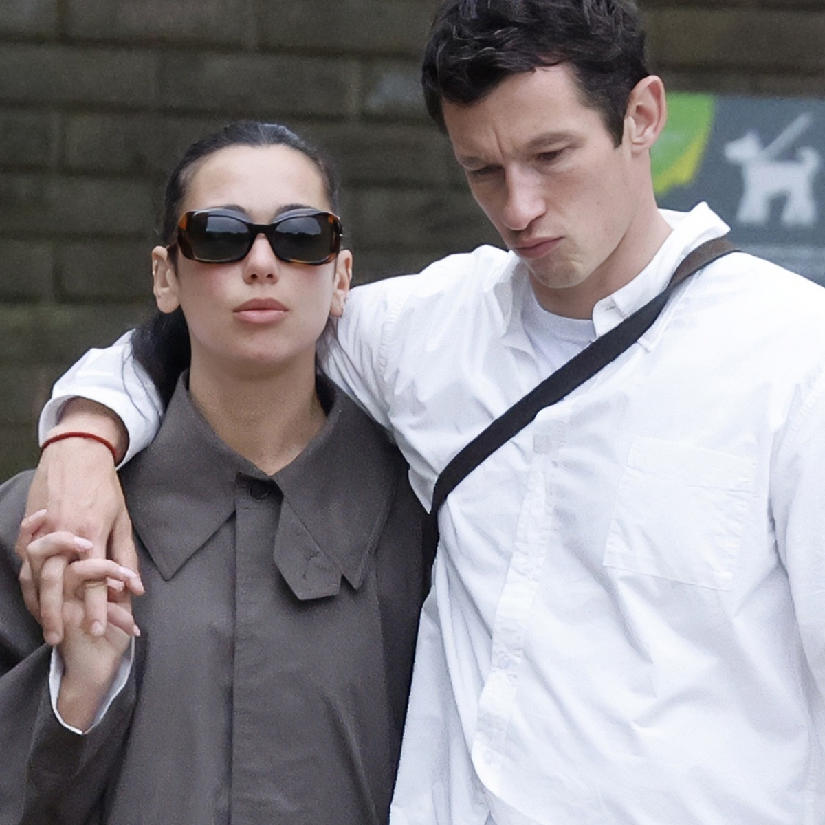 A photo of Dua Lipa and Callum Turner after their London wedding ceremony walking around the city together. Dua is wearing a gray, long trench coat, white jeans, and chestnut Ugg boots.