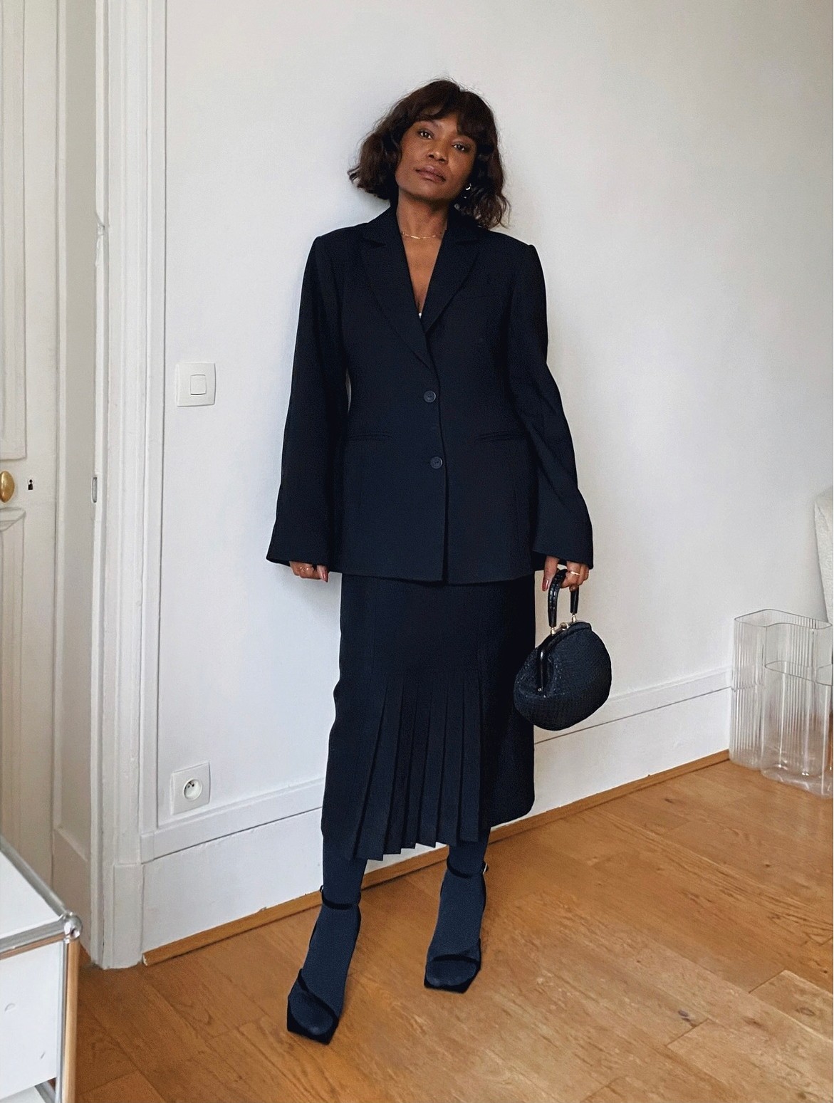 An image of @frannfyne wearing a black pleated skirt with a black blazer.
