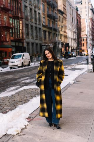 Julia Marzovilla wearing a yellow and black coat, black sweater, jeans, and black boots