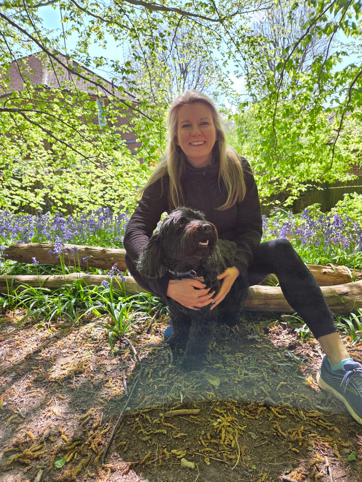 photo of a smiling woman with long blond hair outside in a garden with a small dog