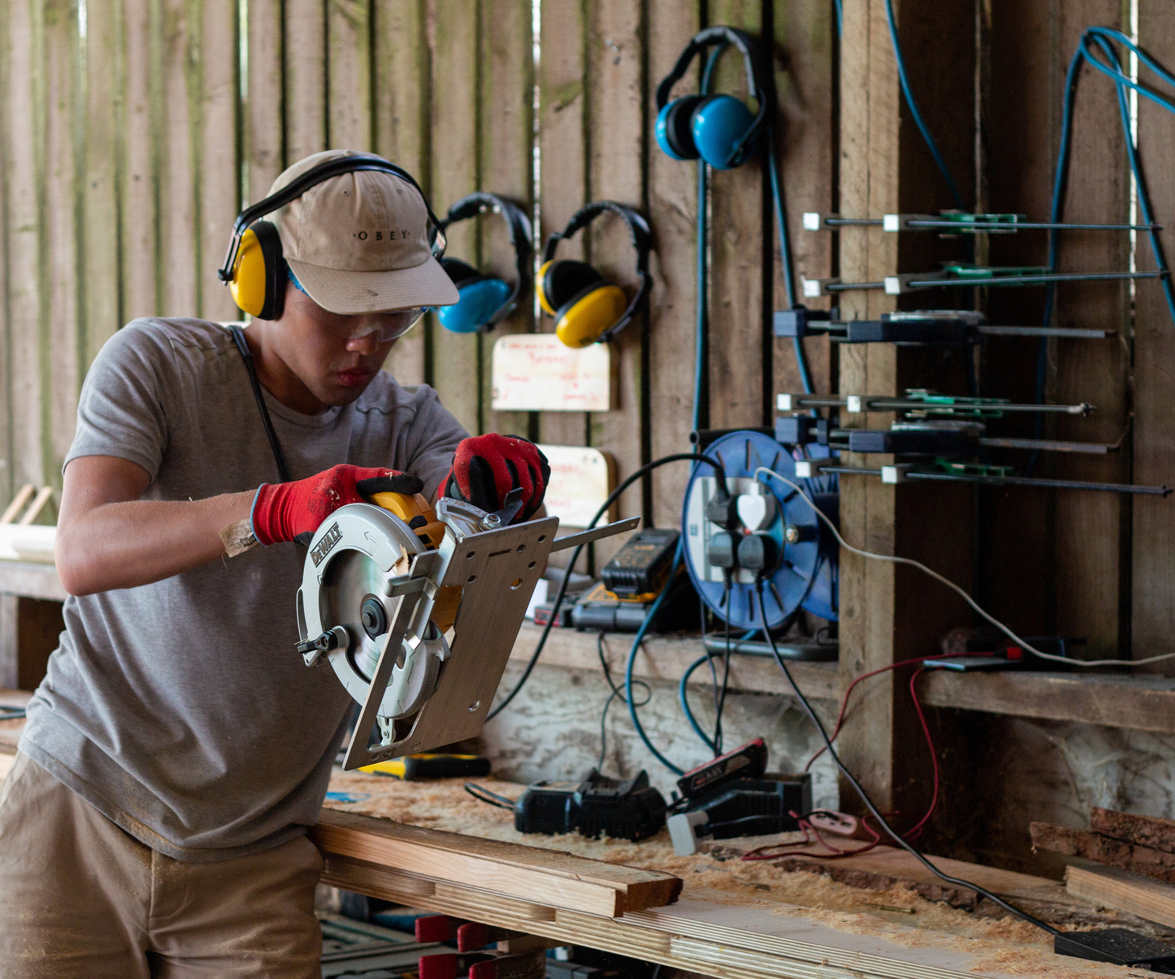 Young construction worker wearing protective ear and eyewear works with a saw to cut planks of wood
