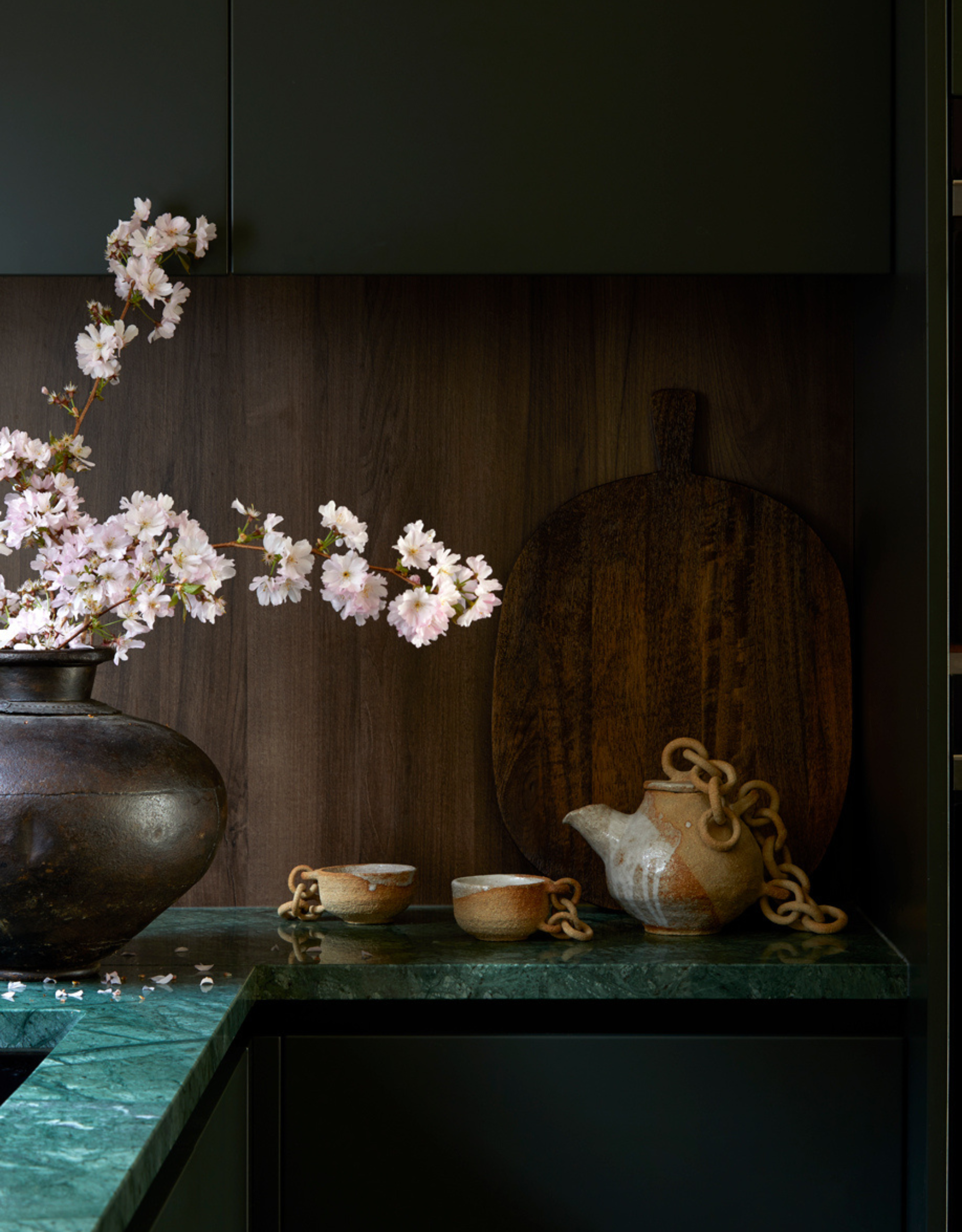 A kitchen with a dark wood backsplash and a bright green marble counter with a ceramic tea set and a vase of flowers