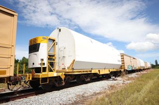 Train cars carry white cylinders on tracks