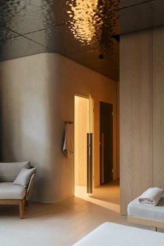 A sauna relaxation room featuring light wood-panelled walls and a polished hammered steel ceiling