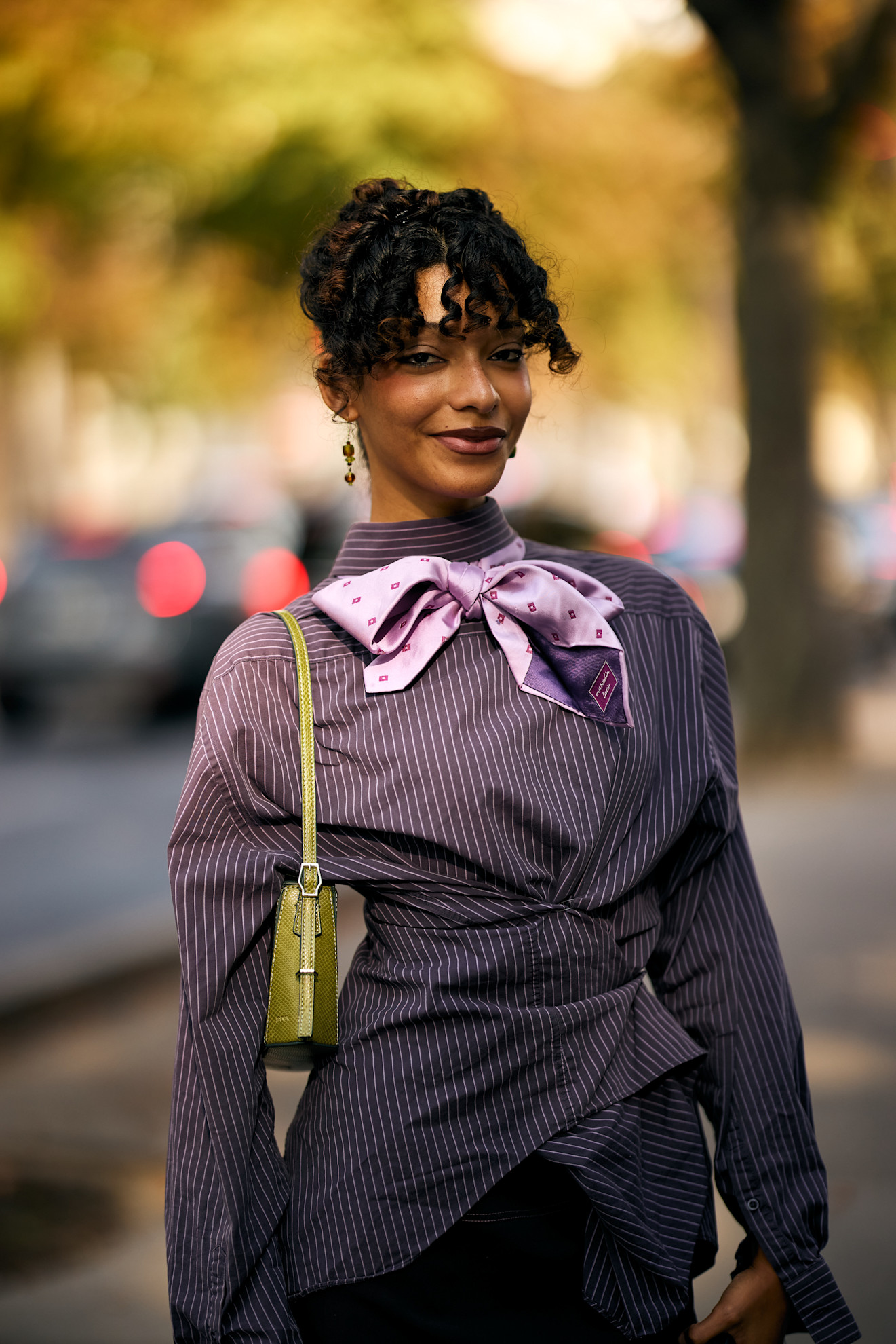 a black woman with curly bangs in a purple dress with a green bag