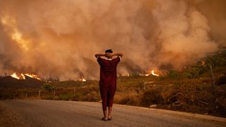 Женщина смотрит на лесные пожары, бушующие в лесу в районе Шефшауэн на севере Марокко, 15 августа 2021 года. Одним из последствий глобального потепления станет усиление волн тепла в некоторых районах, что является фактором риска возникновения лесных пожаров. 