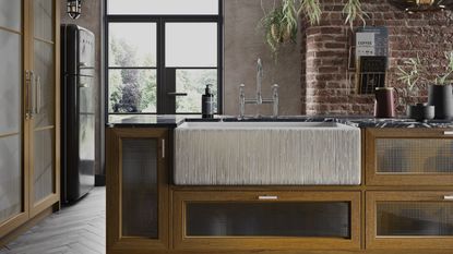 A large textured farmhouse kitchen sink fitted into a wooden cabinet unit in an industrial style kitchen