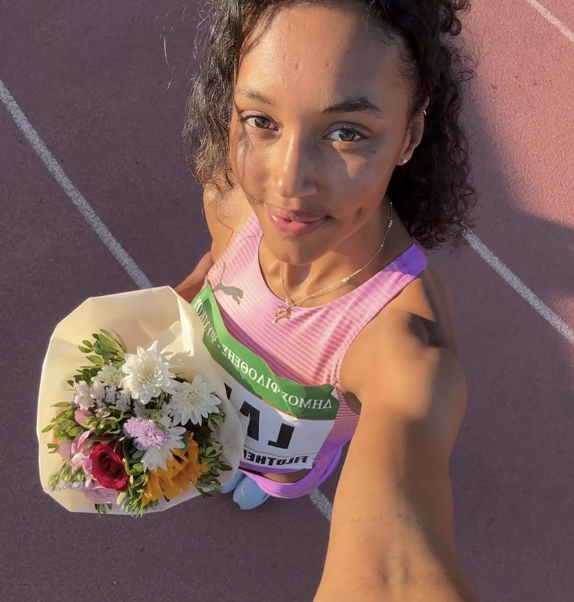 A woman takes a selfie holding a bunch of flowers on an athletics track