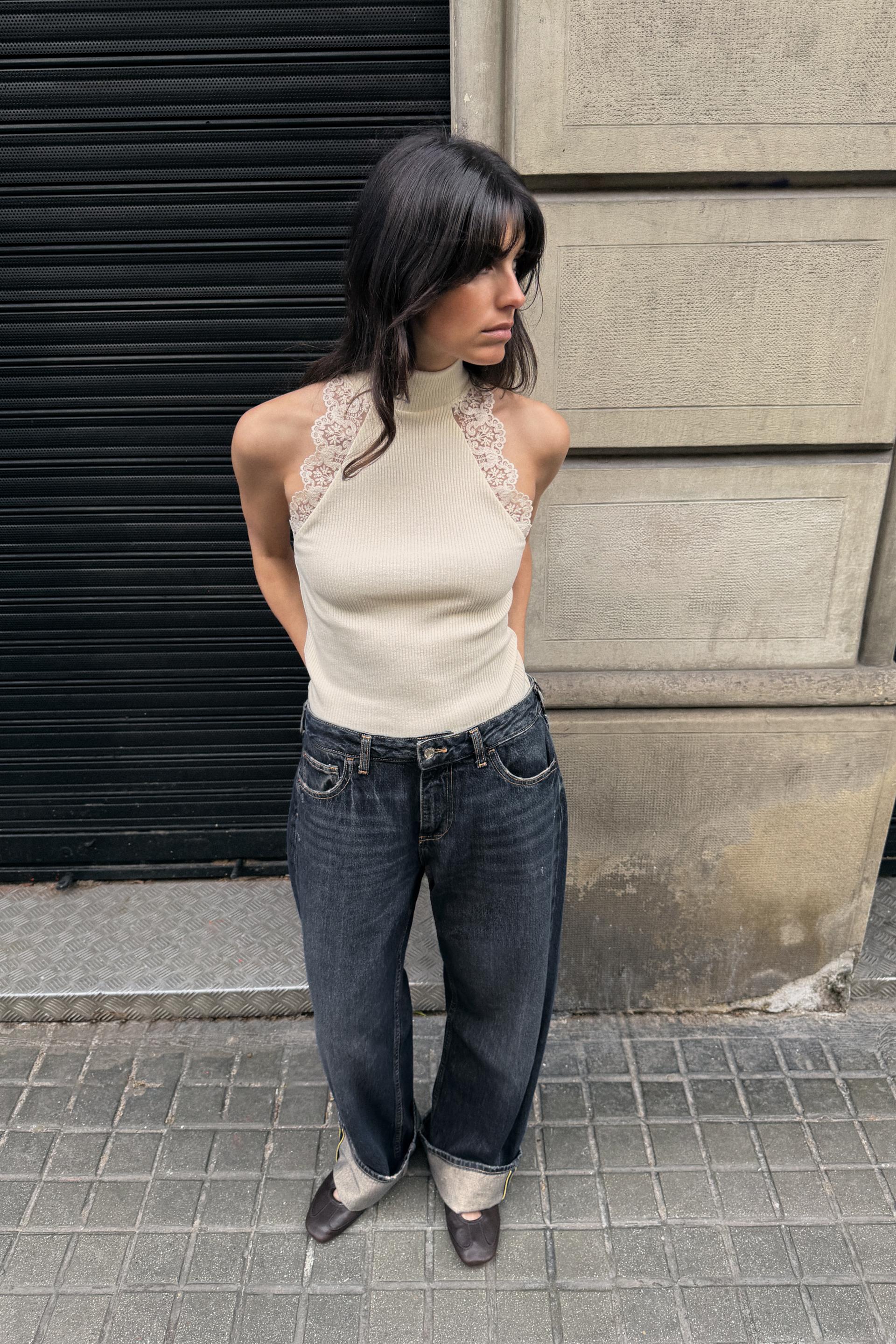 Zara model wearing a sleeveless turtleneck top with lace trim, cuffed dark-wash jeans and brown ballet flats.