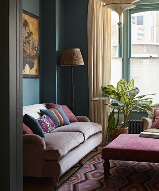 teal living room with pale pink couch, plum footstool, cream drapes, floor lamp, plant, artwork, antique style rug