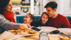 Family with two kids eating dinner in restaurant and paying with smartphone