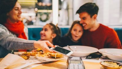 Family with two kids eating dinner in restaurant and paying with smartphone
