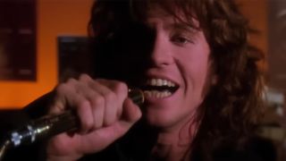 A close up of Val Kilmer as Jim Morrison singing into a microphone in The Doors