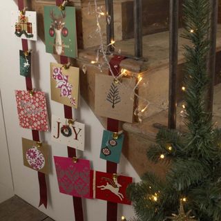 Christmas cards pinned to thick maroon ribbons, hanging down wooden staircase with black balustrades decorated with greenery and fairy lights
