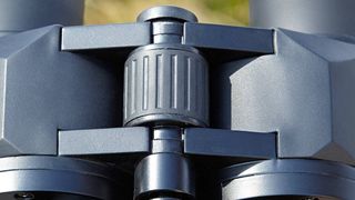 Close-up of the central focusing wheel on a pair of black binoculars.