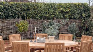 round outdoor dining table with willow screening and tall hedge