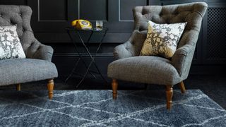 Dark painted living room with grey buttoned armchairs on a thick pile navy blue rug to demonstrate how to make a home cozy in winter