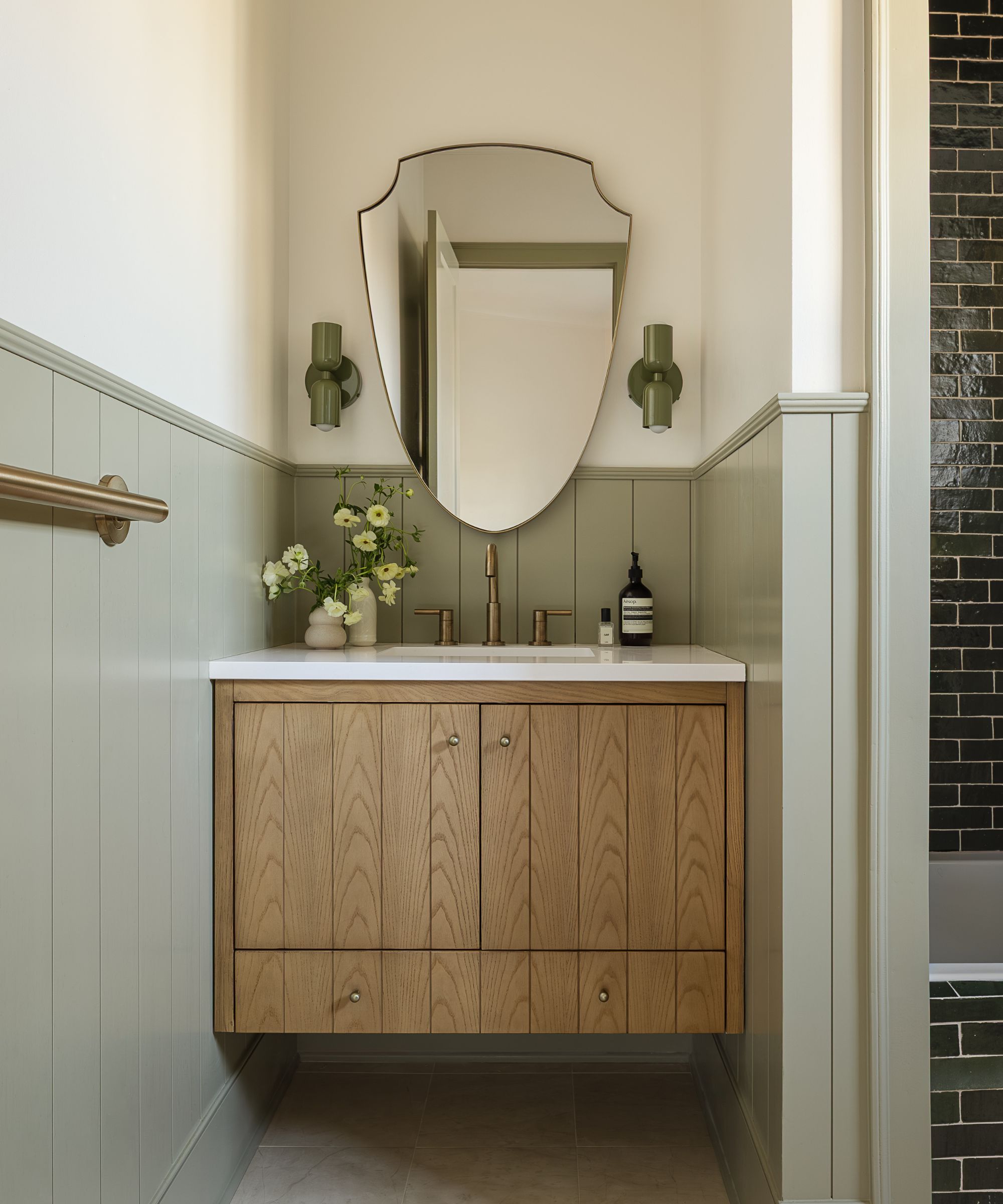 a pistachio green and neutral bathroom with floating wooden vanity and arched mirror