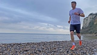 Male runner wearing adidas Terrex Agravic Trail Running T-Shirt, adidas Terrex Heat.Rdy Trail Running Speed Ankle Socks and adidas Terrex trail running shoes on a pebbly beach