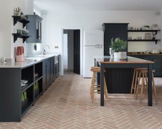 Terracotta floor tiles in modern rustic kitchen scheme, with black cabinets and island.