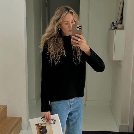 Woman wearing black cashmere sweater and jeans, taking mirror selfie.