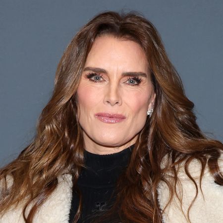 Brooke Shields has long brown wavy hair and wearing a shearling jacket with a black top