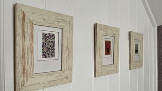 Three embroidered card framed in white washed frames on a tongue and groove wall