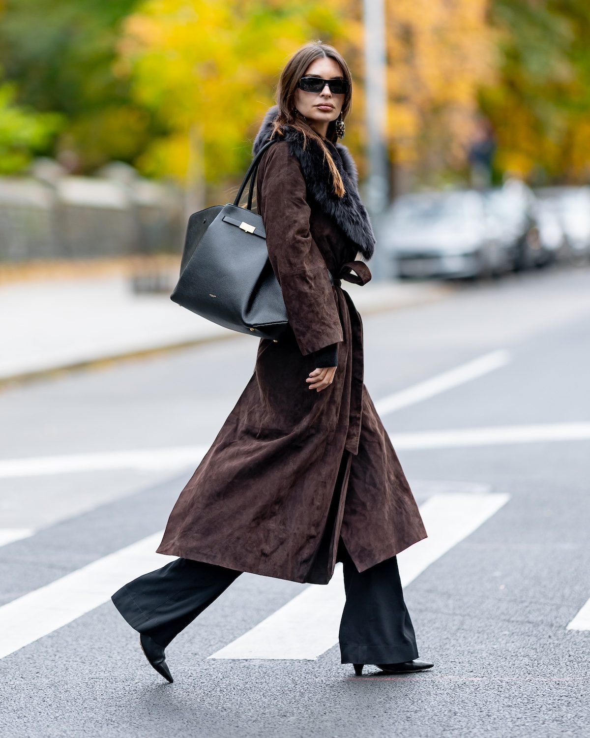 Emily Ratajkowski out in NYC wearing a Demellier New York bag, brown suede belted jacket with a fur collar, wide-leg pants, and black pointed-toe boots
